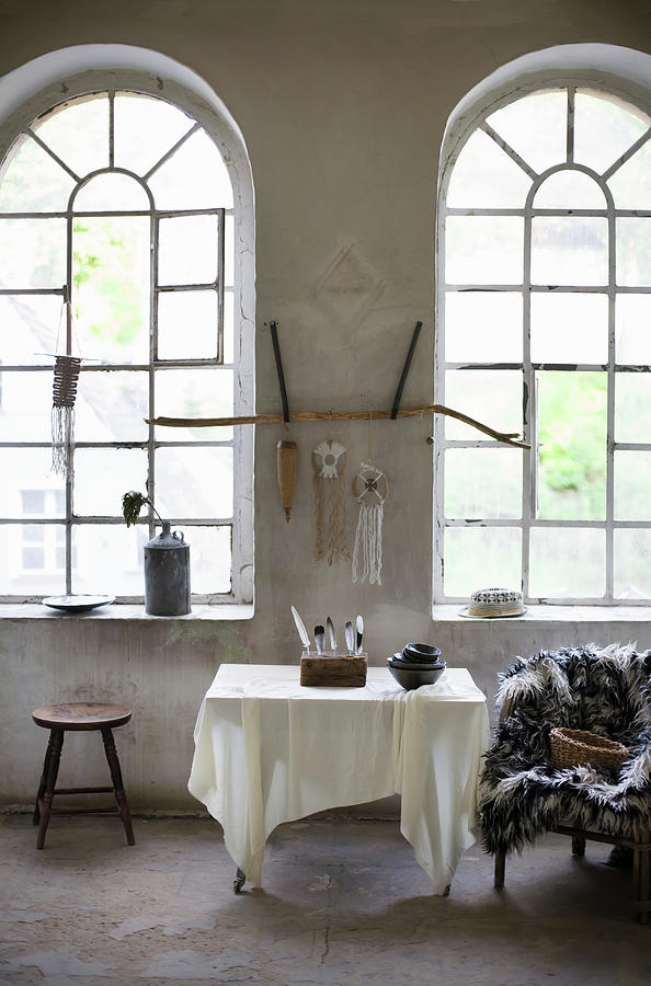 Bowls And Collection Of Feathers On Table, Furry Blanket On Chair And Stool Below Arched Windows In Loft Apartment Photograph by Alicja Koll