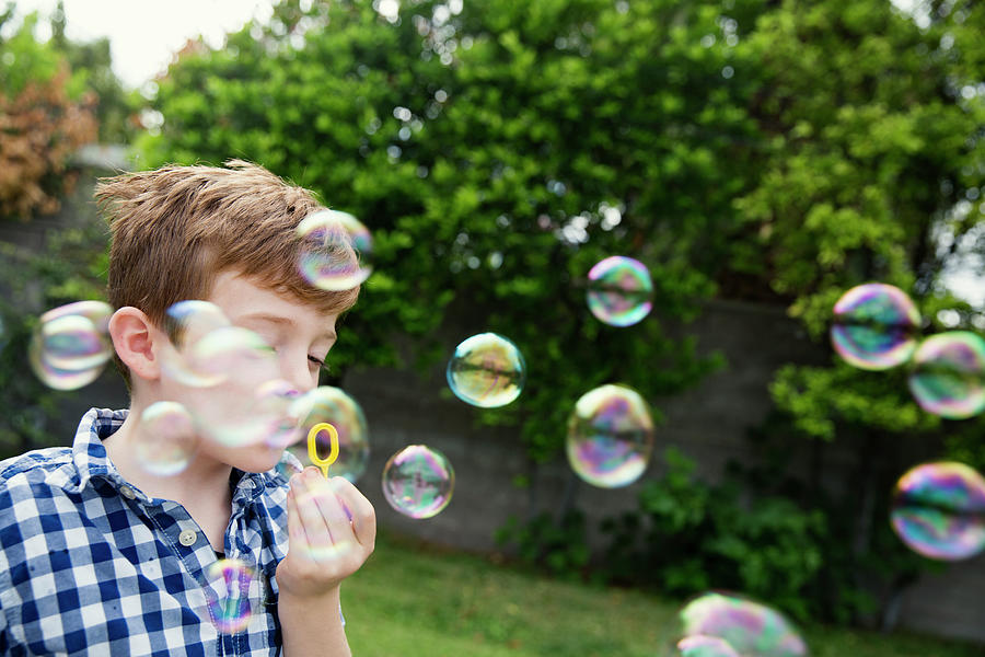 Tree Photograph - Boy Blowing Bubbles In Yard by Cavan Images