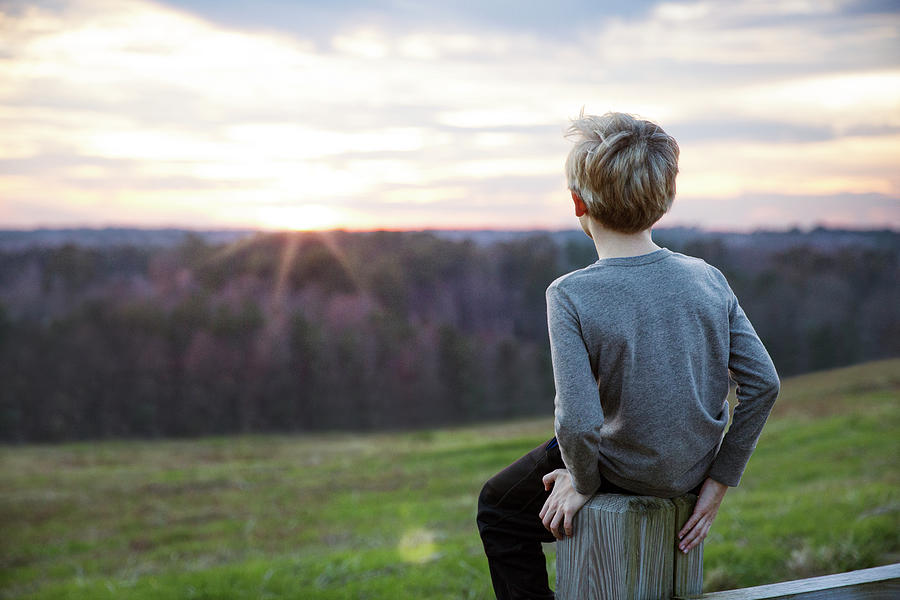 Boy Looking At Sunset Sitting On Fence Photograph by Cavan Images ...