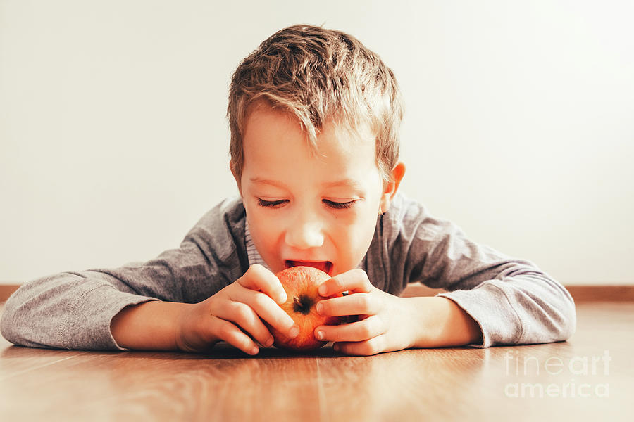 Boy lying down biting an apple, isolating white background, conc Photograph by Joaquin Corbalan