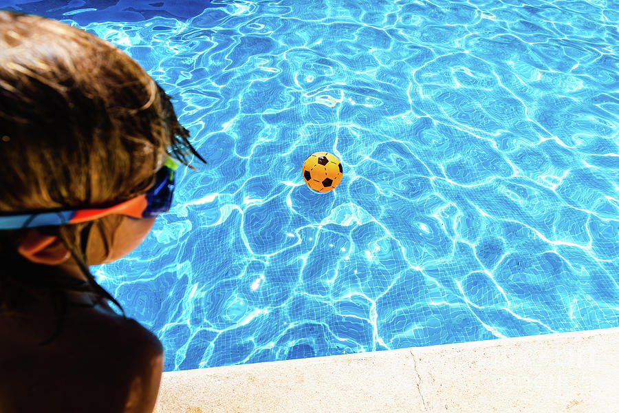 Boy observing a ball moving away from him in a pool in summer, c Photograph by Joaquin Corbalan