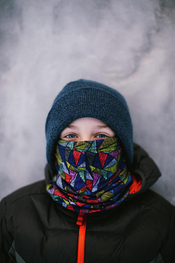 Winter Photograph - Boy With Blue Eyes Lays In Snow With Beanie, Neck Warmer And Ski Coat by Cavan Images / Anna Rasmussen Photographs
