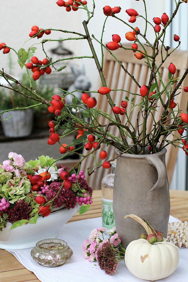 Branches Of Rose Hips In Stoneware Jar Next To Autumnal Flowers Photograph by Erika Reetz