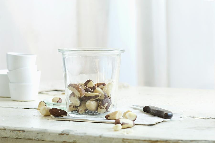 Brazil Nuts In And Next To A Glass Jar On A Rustic Kitchen Table Photograph by Achim Sass