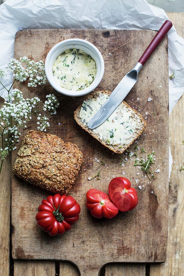 Bread With Herb Butter And Tomatoes On An Old Chopping Board Photograph by Sabine Steffens