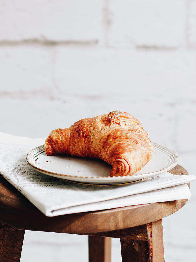 Breakfast Croissant And Newspaper On A Wooden Stool Photograph by Paulina Sauer