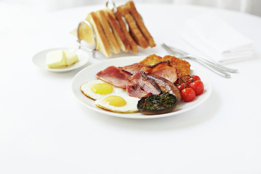Breakfast Of Fried Eggs, Bacon, Sausages, Fried Mushrooms, Hash Browns And Tomatoes Served With A Rack Of Toast Photograph by Charlotte Tolhurst