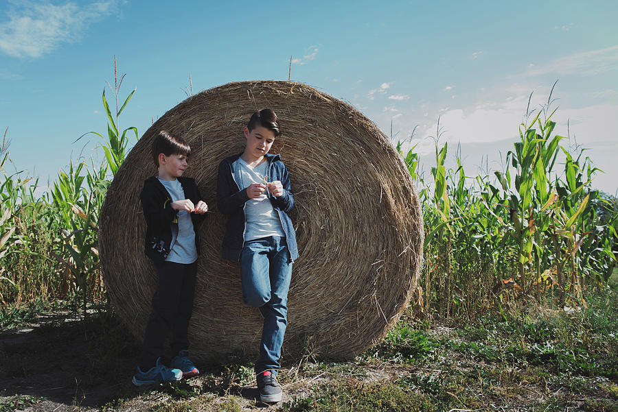 Nature Photograph - Brothers Standing By Hay Bale In Corn Field Against Sky by Cavan Images