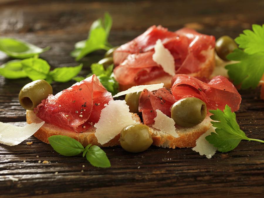 Bruschetta Topped With Bresaola, Green Olives And Parmesan Shavings Photograph by Robert Morris