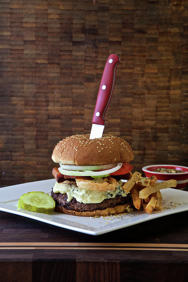 Burger With Blue Cheese, Lettuce, Deep Fried Onions, Fries, Pickle And Tomato On A Dark Rustic Background With A Knife Photograph by Andre Baranowski