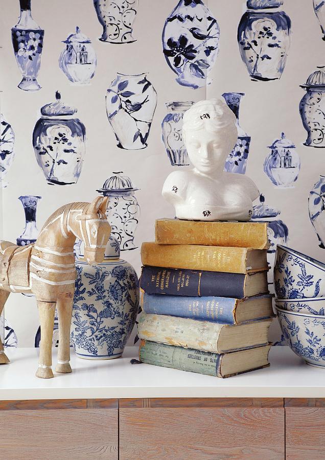 Bust Of Woman On Stacked Books, Blue And White Painted Ceramic Vase And Bowls In Front Of Wallpaper With Pattern Of Vases Photograph by Great Stock!