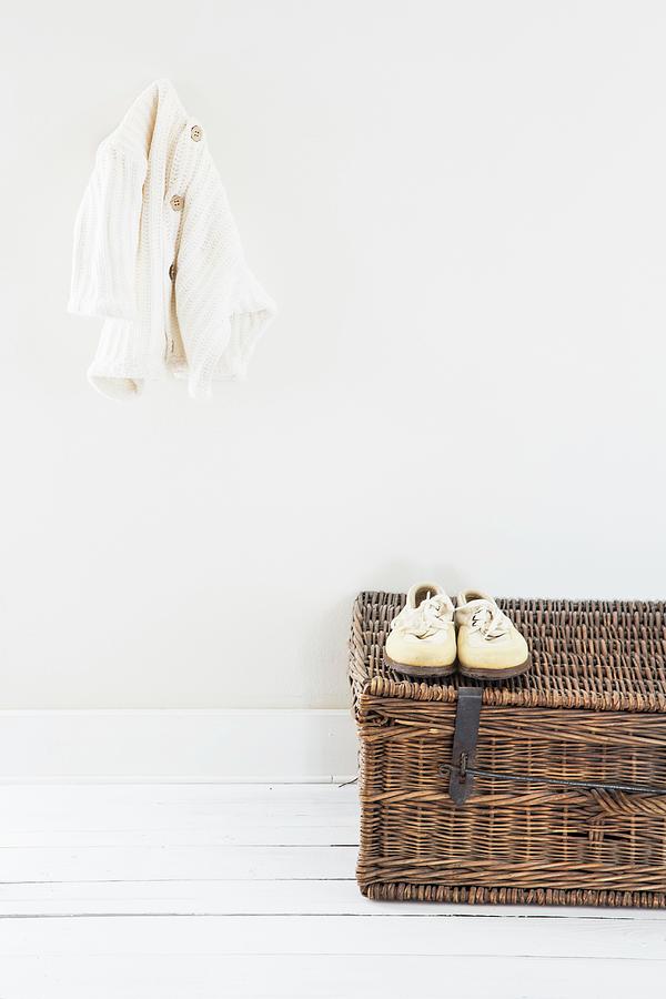 Cardigan Hung On Wall Above White Shoes On Wicker Trunk Photograph by Catja Vedder