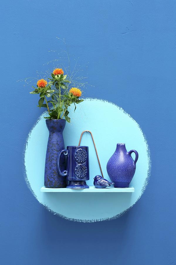 Ceramic Vessels And Flowers On Wall-mounted Shelf In Pale Blue Circle On Rich Blue Wall Photograph by Thordis Rggeberg