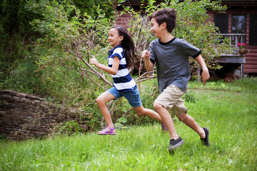 Cheerful Siblings Running On Grassy Field In Front Yard Photograph by ...