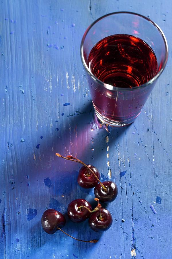 Cherries And Cherry Juice On A Blue Wooden Tabletop Photograph by Mandy Reschke