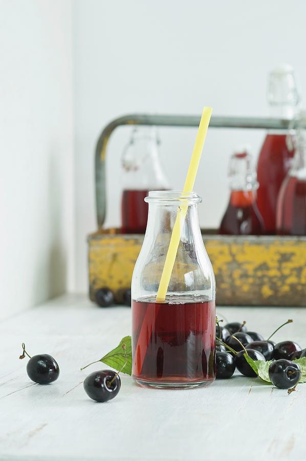 Cherry Juice In A Glass Bottle With A Straw, Bottles In A Bottle Carrier And Fresh Cherries Photograph by Achim Sass