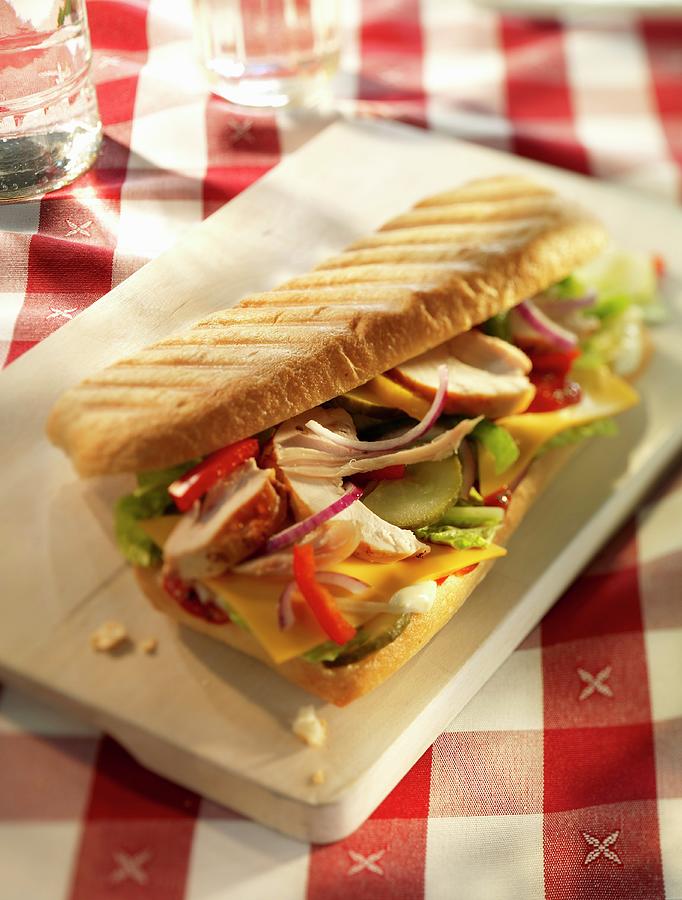 Chicken, Onion, Pepper, Gherkins, Cheese Slices, Lettuce And Ketchup In A Baguette On A Wooden Board Photograph by Hebra