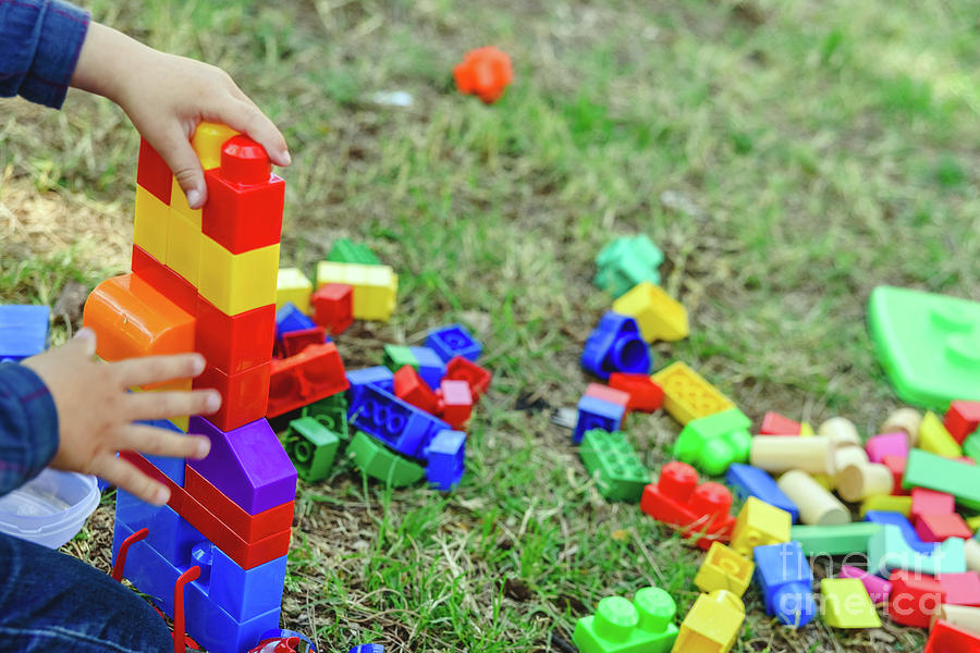 Child playing with colorful blocks sitting on the ground of a garden in spring, negative space. Photograph by Joaquin Corbalan