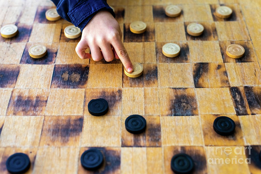Childs hands moving pieces of Checkers game, concepts of struggle, strategy and confrontation. Photograph by Joaquin Corbalan