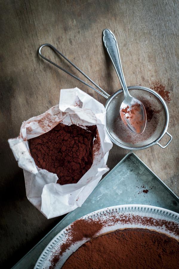 Chocolate Cake On A Metal Tray With Utensils For Sprinkling Cocoa Powder On A Wooden Table Photograph by Food With A View