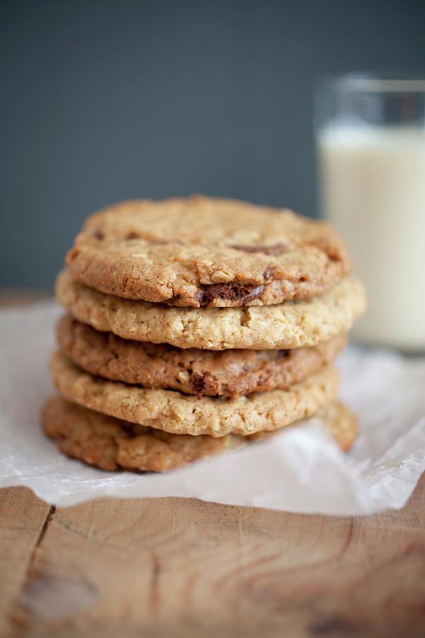 Chocolate Chip, Peanut Butter And Oatmeal Cookies Stacked On Baking Parchment Wih A Glass Of Milk In The Background. Photograph by Harley, Victoria