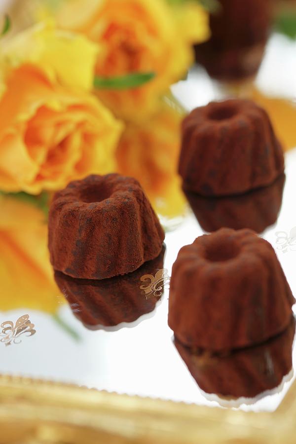 Chocolate Pralines On A Mirrored Tray With Orange Coloured Roses In The Background Photograph by Angelica Linnhoff