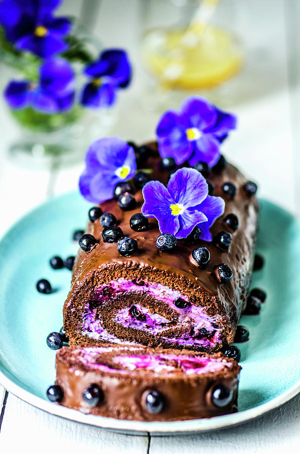 Chocolate Roll With Cream And Blueberries, Decorated With Violet Flowers On A Blue Plate Photograph by Gorobina