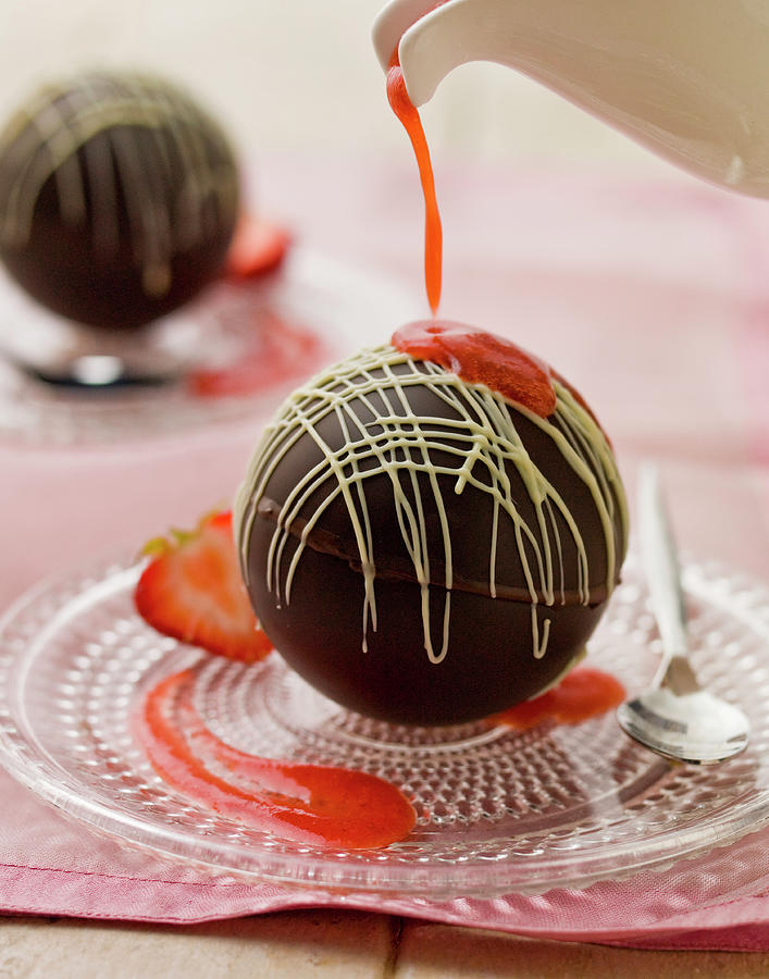 Chocolate Spheres With Melting Hot Strawberry Sauce Being Poured From A White Jug, On A Glass Plate And Spoon Photograph by Clive Sherlock