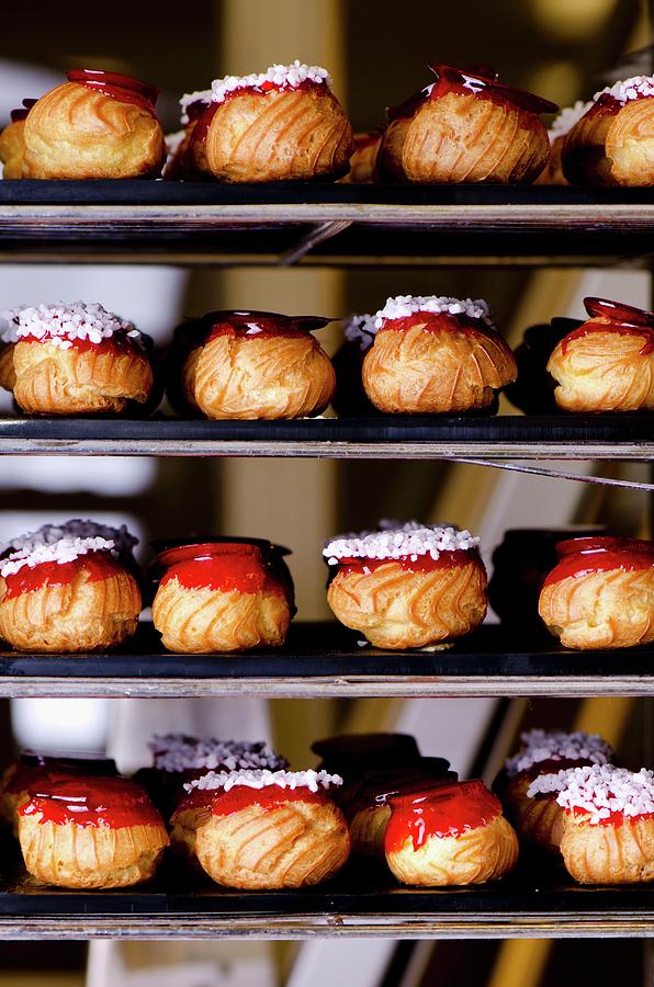 Choux Buns With Red Caramel Topping And Sugar Crystals On Shelves In A Bakery Photograph by Jamie Watson