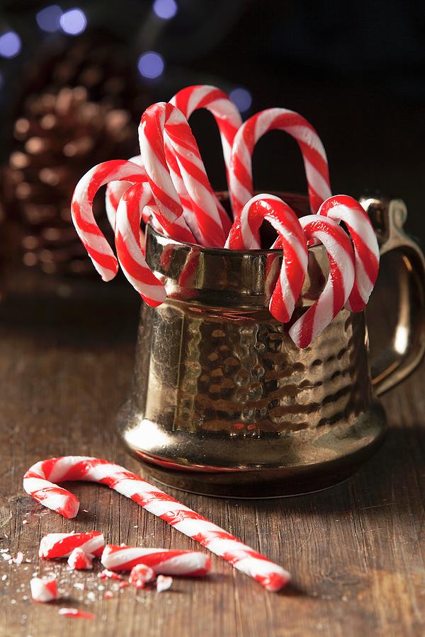 Christmas Candy Cane In A Traditional Style Gold Mug With One Whole Can On The Table With Broken Candy Can Pieces Photograph by Stacy Grant