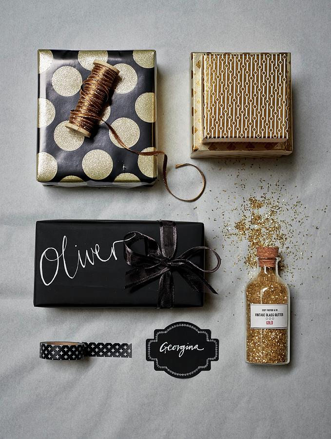 Christmas Gifts Wrapped In Black And Gold Paper With Matching Ribbons Arranged With Gold Glitter Photograph by Catherine Gratwicke