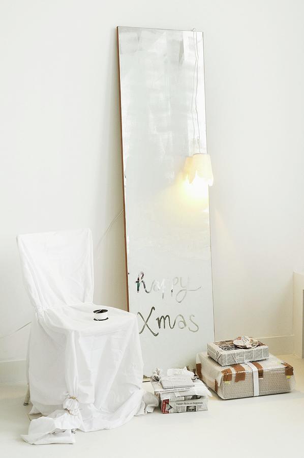 Christmas Greeting On Dull Mirror, Loose-covered Chair And Gifts Wrapped In Newspaper Photograph by James Stokes