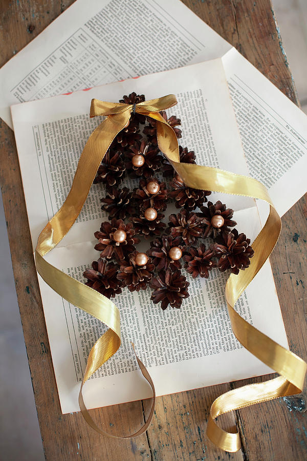 Christmas-tree Shape Made From Pine Cones And Beads With Gold Ribbon On Book Pages Photograph by Alicja Koll