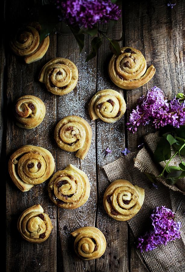 Cinnamon Rolls On A Wooden Background, With Violet Lilac Flowers Photograph by Laura Negrato