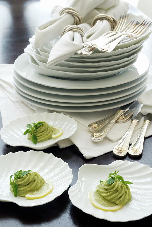 Clamshell-shaped Dishes With Avocado Pure In Front Of A Stack Of Plates And Napkins In Silver Rings Photograph by Blickpunkte