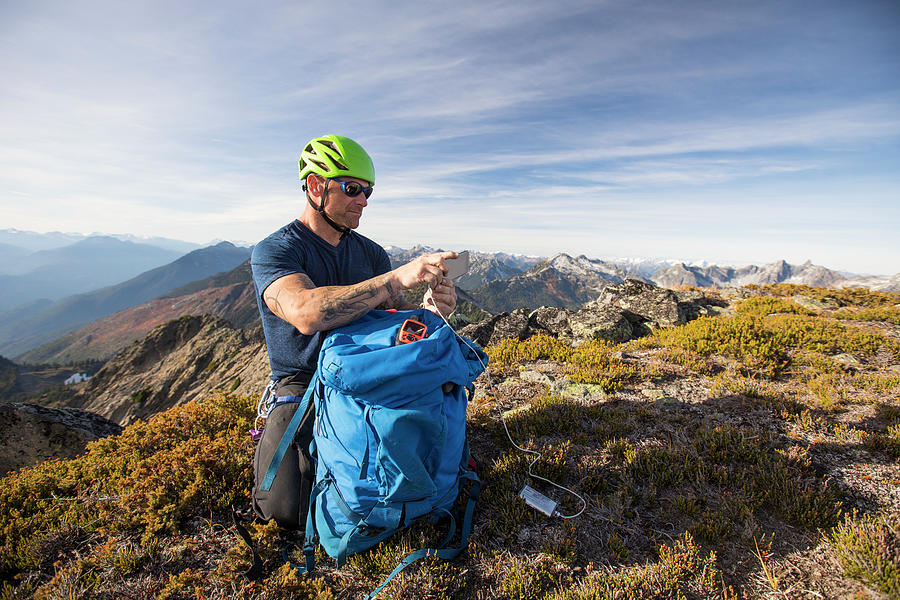 Nature Photograph - Climber Charges His Phone With Battery Pack On Mountain Summit. by Cavan Images