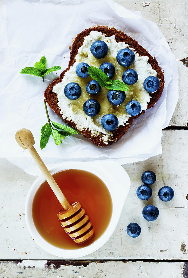 Close Up Of Grunge White Wooden Table With Ricotta, Fresh Blueberries And Honey Sandwich On Whole Grain Bread Photograph by Yuliya Gontar