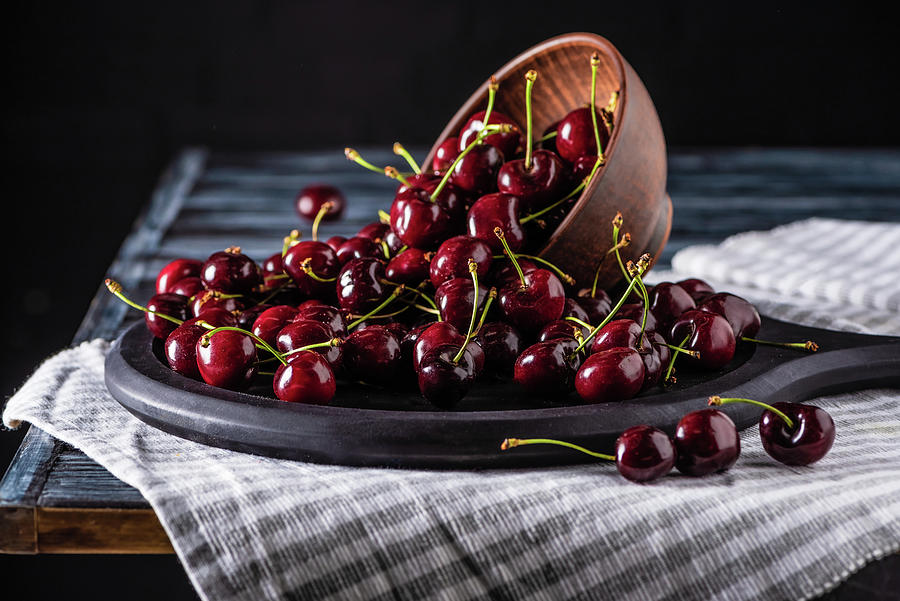 Close Up View Of Pile Of Red Ripe Cherries In Bowl On Cutting Board On Wooden Table Photograph by Lightfield Studios