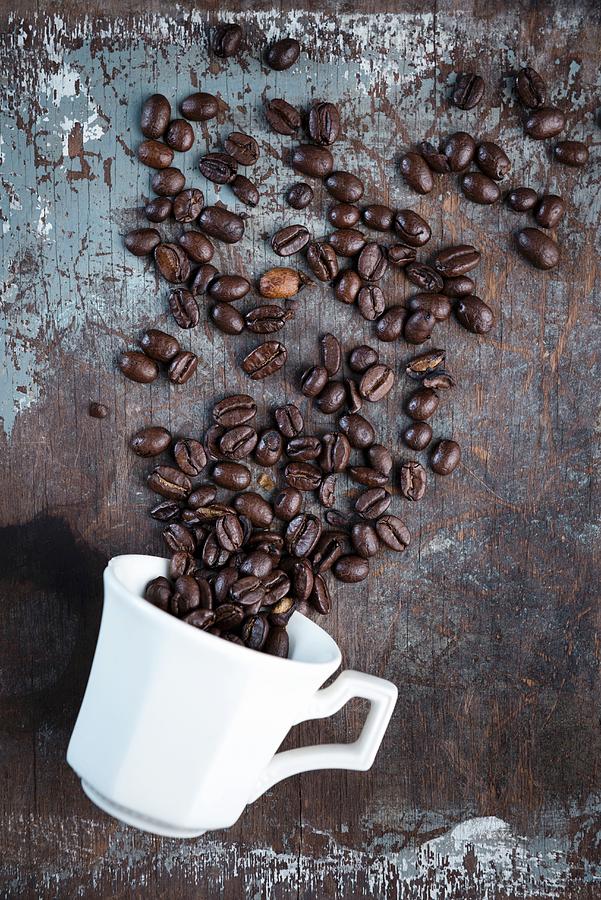 Coffee Beans Scattered Over A Rustic Surface With A White Coffee Cup Photograph by Komar