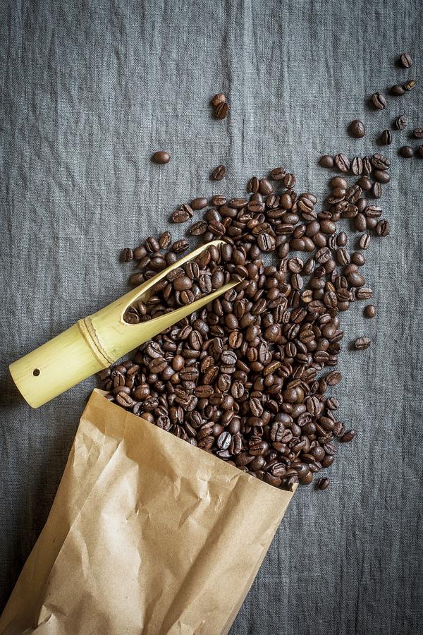 Coffee Beans Spilling From A Paper Bag With A Bamboo Scoop On A Grey Linen Cloth Photograph by Food With A View