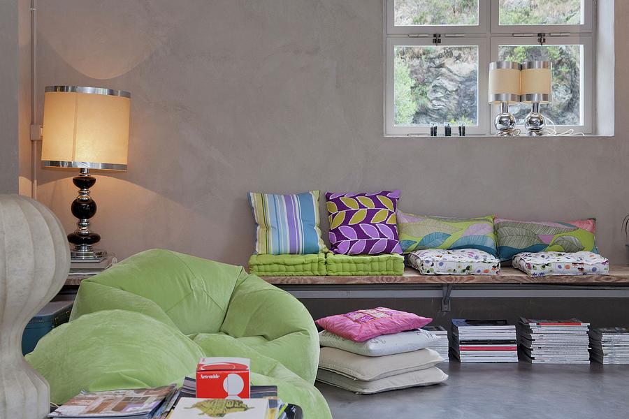 Collection Of Colourful Cushions On Wall-mounted Bench, Lime Green Beanbag Chairs And Postmodern Table Lamps Contrasting With Cool Exposed Concrete Of Loft Interior Photograph by Fabio Lombrici