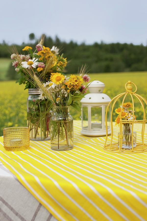 Colourful Bouquets Of Wildflowers In Vintage Jars, Ornamental Bird Cage And Lantern On Yellow And White Striped Tablecloth Outdoors Photograph by Annette Nordstrom