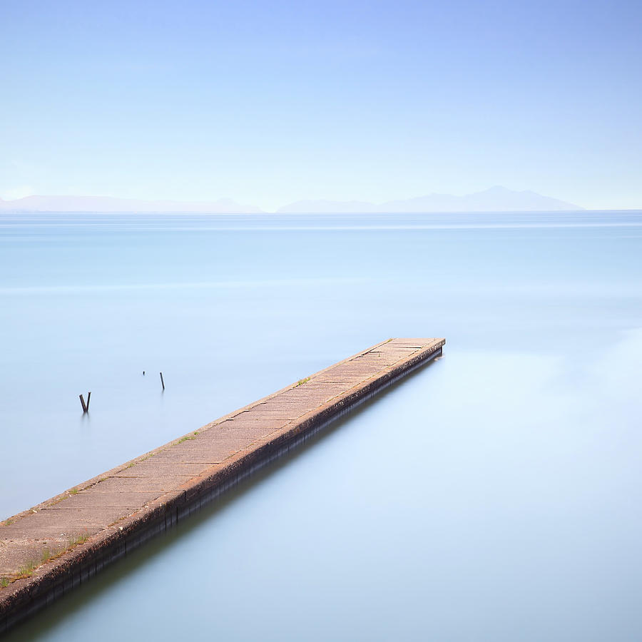 Concrete pier or jetty on a blue sea. Hills on background Photograph by Stefano Orazzini
