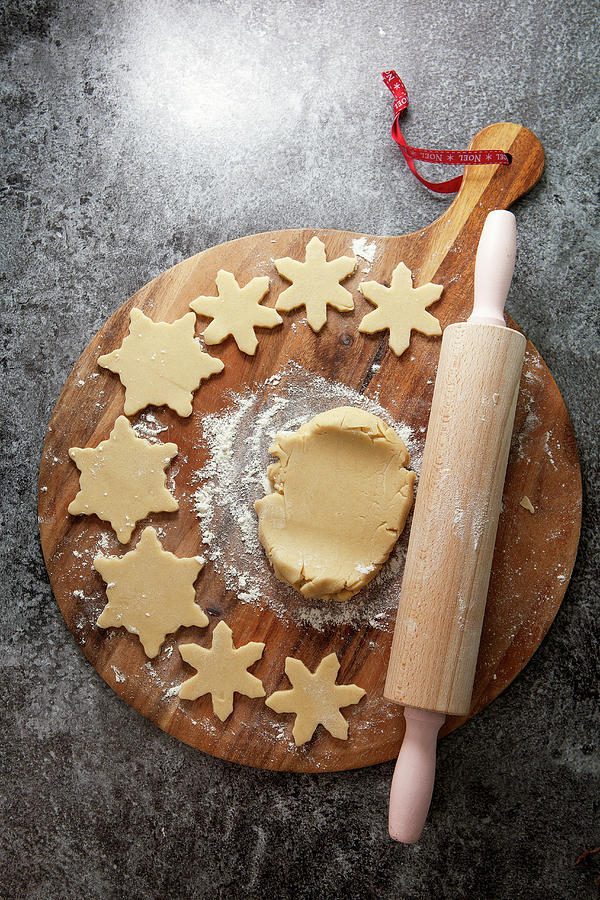 Cookie Dough On A Floured Wooden Chopping Board Surrounded With Cutter Out Snowflake Shapped Biscuits Next To A Rolling Pin On A Grey Slate Background Photograph by Stacy Grant