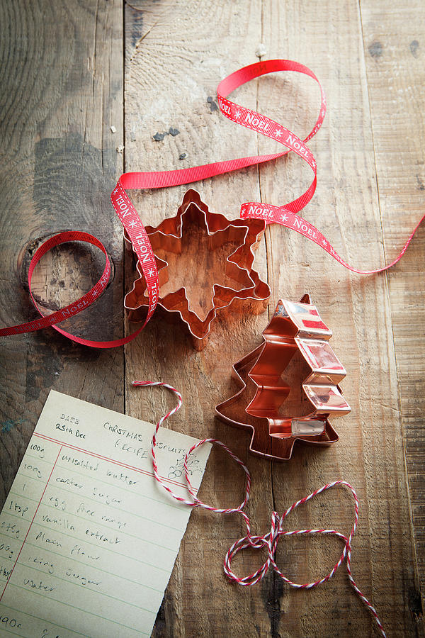 Copper Christmas Shaped Cookie Cutters On A Rustic Wooden Surface With Red Noel Ribbon Bakers Twine And Cookie Recipe Photograph by Stacy Grant