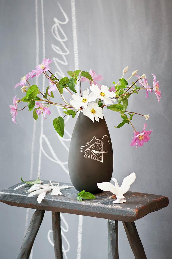Cosmea In Dark Grey Retro Vase On Old Wooden Stool In Front Of Grey Wall Photograph by Cornelia Weber