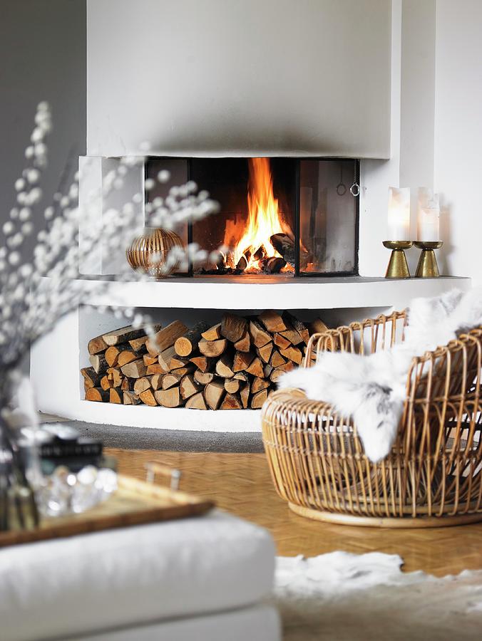 Cosy Basketwork Armchair With White Fur Blanket In Front Of Fire In Open Fireplace With Firewood Store Below Photograph by Stefan Thurmann