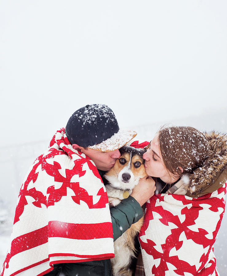 Couple & Dog Huddle In Blanket During Snowfall & Kiss Dog Together Photograph by Cavan Images