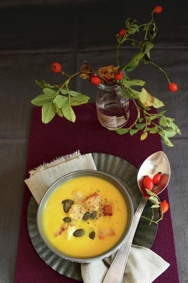 Cream Of Pumpkin Soup With Pumpkin Seeds And A Sprig Of Rosehips Decorating The Table Photograph by Regina Hippel