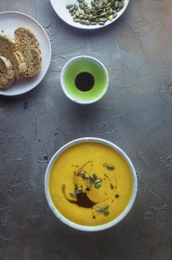 Cream Of Pumpkin Soup With Pumpkin Seeds And Pumpkin Seed Oil On A Grey Surface Photograph by Barbara Pheby